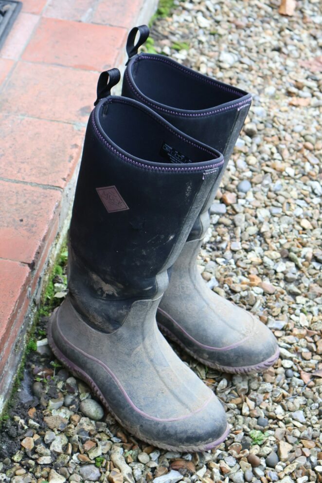 Pair of muddy black rubber boots on gravel.